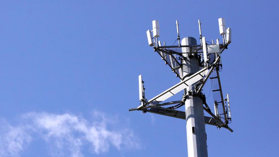 Cell tower sitting against a blue sky with a cloud