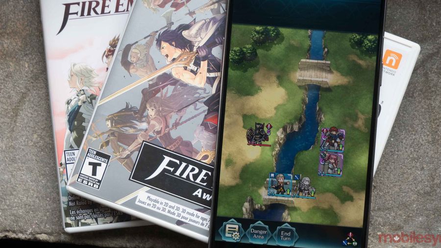 Fire Emblem Heroes playing on a phone that is laying on top of video game cases