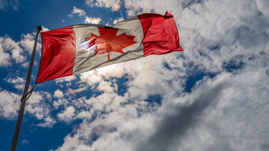 An image of the Canadian flag blowing in the wind against a backdrop of clouds