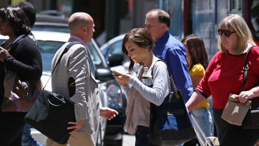 An image showing a woman looking at her phone while crossing the street