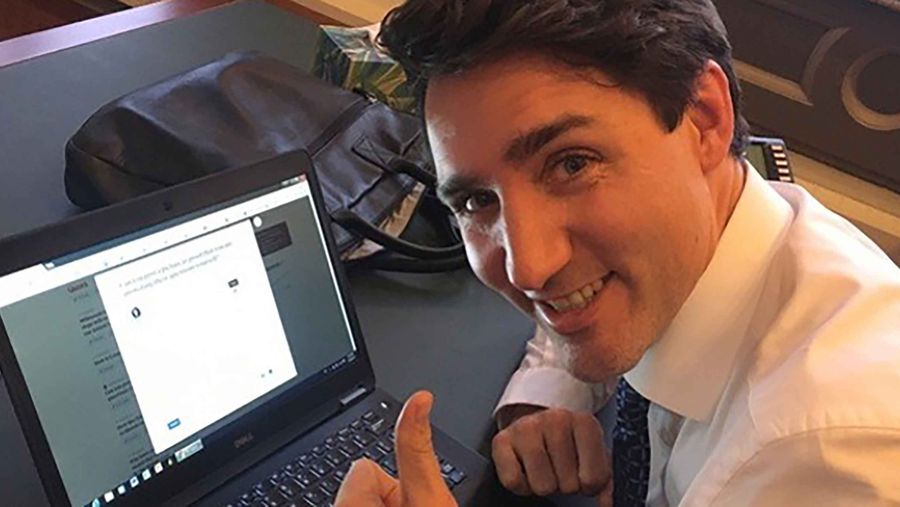 trudeau with his thumbs up beside a laptop.