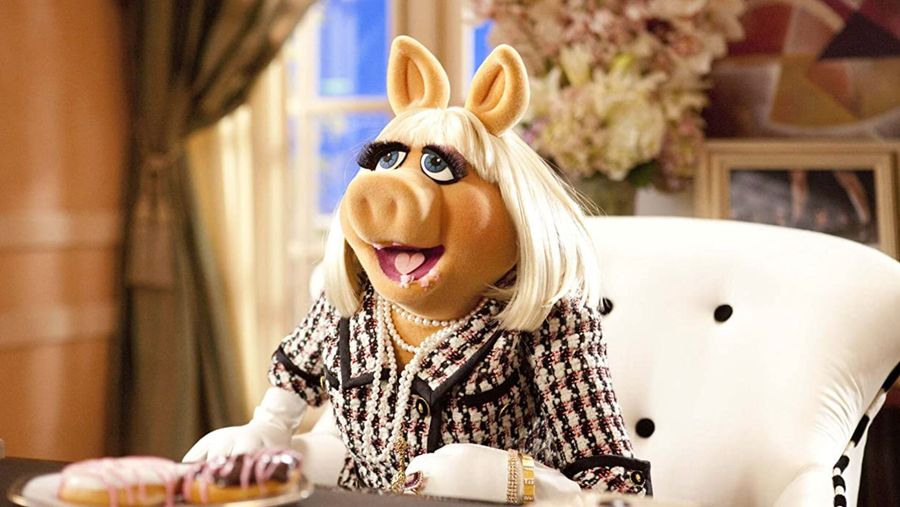 miss piggy's mouth open with donuts in her mouth. She's sitting down on a white chair.